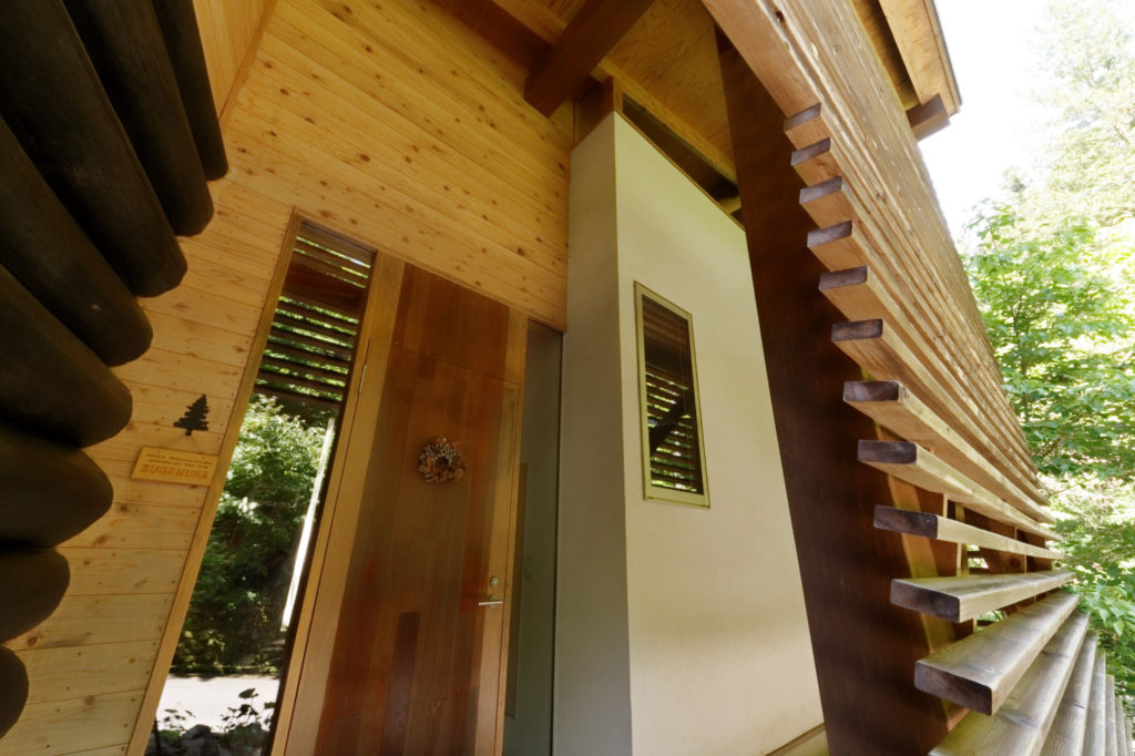 木製ルーバーと漆黒の丸太を抜けると木製の玄関ドアへ